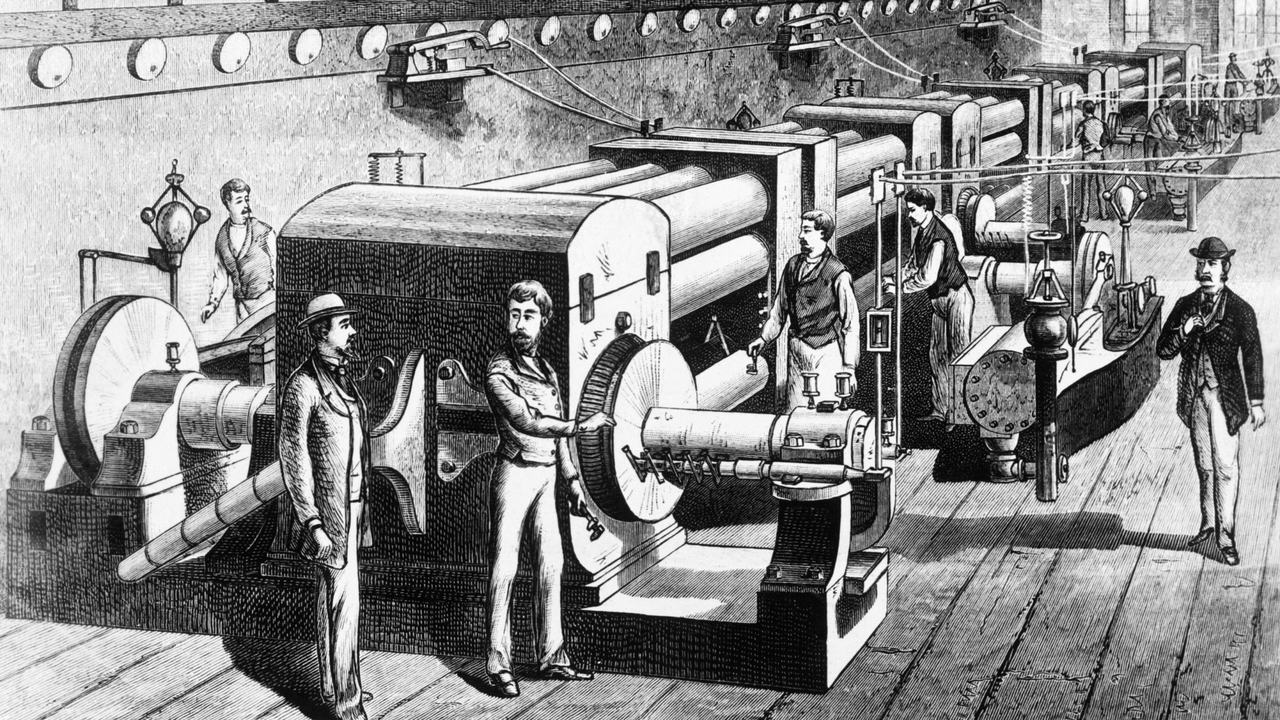 Engraving of the dynamo room at Edison’s Pearl Street station: a row of large steam-driven dynamos, with engineers and visitors on the plank floor.